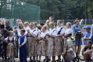 grupa osób, w wiekszości składająca się z członków zespołu regionalnego: dziewczynki ubrane w kolorowe stroje i przyglądające sie występom swoich starszych kolegów