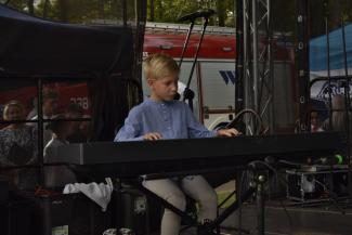 na scenie, chłpiec w niebieskiej koszulce wykonuje utwór na fortepianie
