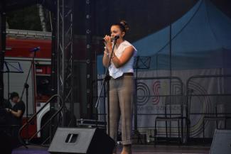 na scenie solistka, ubrana w biała bluzkę i bezowe spodnie, trzymająca mikrofon w ręce, wykonująca utwór