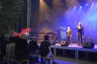 przed scena zgromadzeni ludzie, siedzący na ławkach; na scenie, na fioletowym tle: dwóch mężczyzn: Krzysztof Hanke i Respondek, z kabaretu Rak 