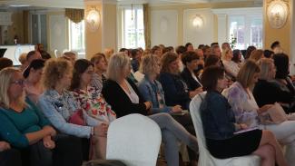 zdjęcie przedstawia zgormadzonych uczestników konferencji, siedzących i słuchających prelegenta