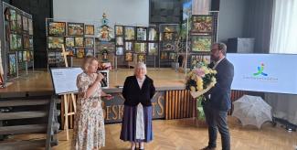 artystce zostaje wręczana nagroda od ministra kultury i dziedzictwa narodowego, kobieta trzyma teczkę, mężczyzna kwiaty