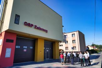 budynek OSP Zabrzeg, w tle grupa ludzi w trakcie odbioru inwestycji
