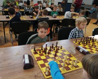 turniej szachowy - osoby siedzą przy długich stołach przed sobą mają szachownice z pionkami i zegary liczące czas