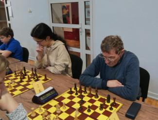 turniej szachowy - osoby siedzą przy długich stołach przed sobą mają szachownice z pionkami i zegary liczące czas
