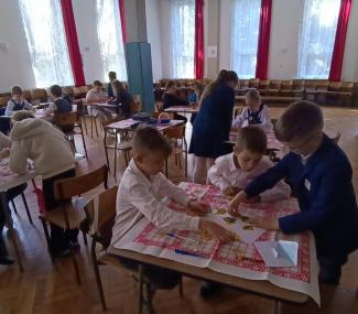 dzieci w trzyosobowych grupach, przy stolikach rozstawionych na szkolnej auli, rozwiązujące zadania konkursowe