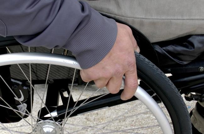 Osoba na wózku inwalidzkim. Zbliżenie na dłoń opartą na obęczy koła. 