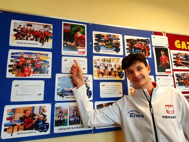 Michał Gawlas wskazujący na swoje zdjęcie na gazetce szkolnej